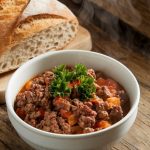 A warm bowl of ground beef crockpot dinner served with crusty bread on the side