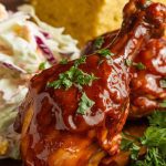 A beautifully plated dish of BBQ chicken drumsticks, glistening with sauce and garnished with fresh parsley