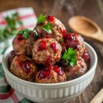 A bowl of cranberry-glazed meatballs garnished with parsley