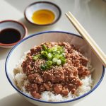 a plated serving of Asian ground beef over white rice, garnished with sesame seeds and green onions