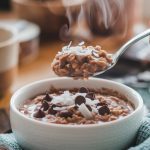 A bowl of steaming chocolate coconut oatmeal topped with shredded coconut and mini chocolate chips