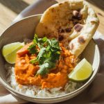 A bowl of sweet potato curry served over steamed jasmine rice, topped with fresh cilantro and lime wedges