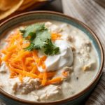 a bowl of creamy white chicken chili topped with cheese, sour cream