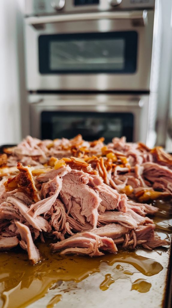 Shredded pork on a baking sheet, golden and crispy around the edges with drizzled juices