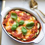 Cooked crockpot zucchini lasagna garnished with fresh basil leaves, served in a white dish