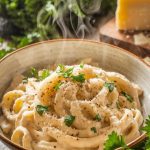 A plate of creamy chicken Alfredo garnished with Parmesan and parsley