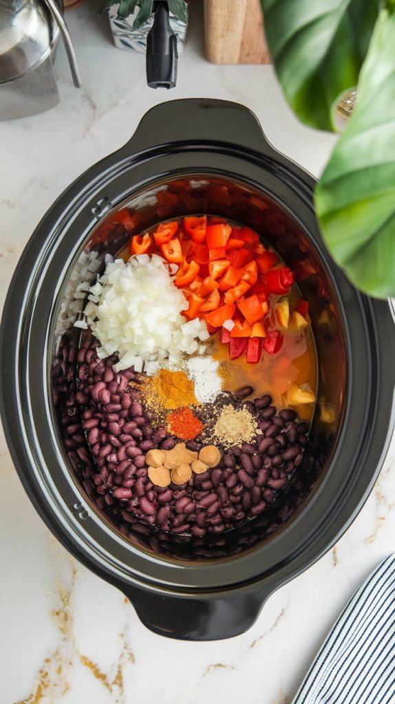 A Crockpot filled with black beans, vegetable broth, diced onion, red bell pepper, garlic, canned tomatoes