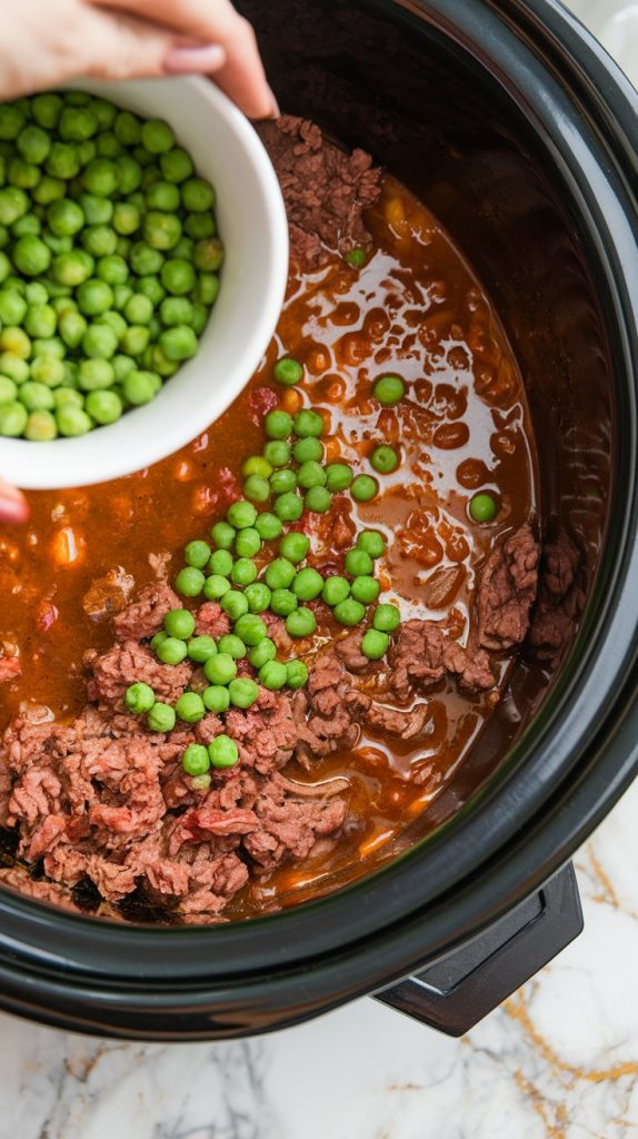 A crockpot filled with hearty ground beef stew, vibrant green peas being stirred in