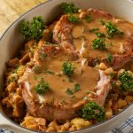 A serving of crockpot pork chops plated with stuffing and sprinkled with fresh parsley