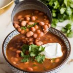 a ladle pouring pinto bean soup into a bowl, with chopped cilantro