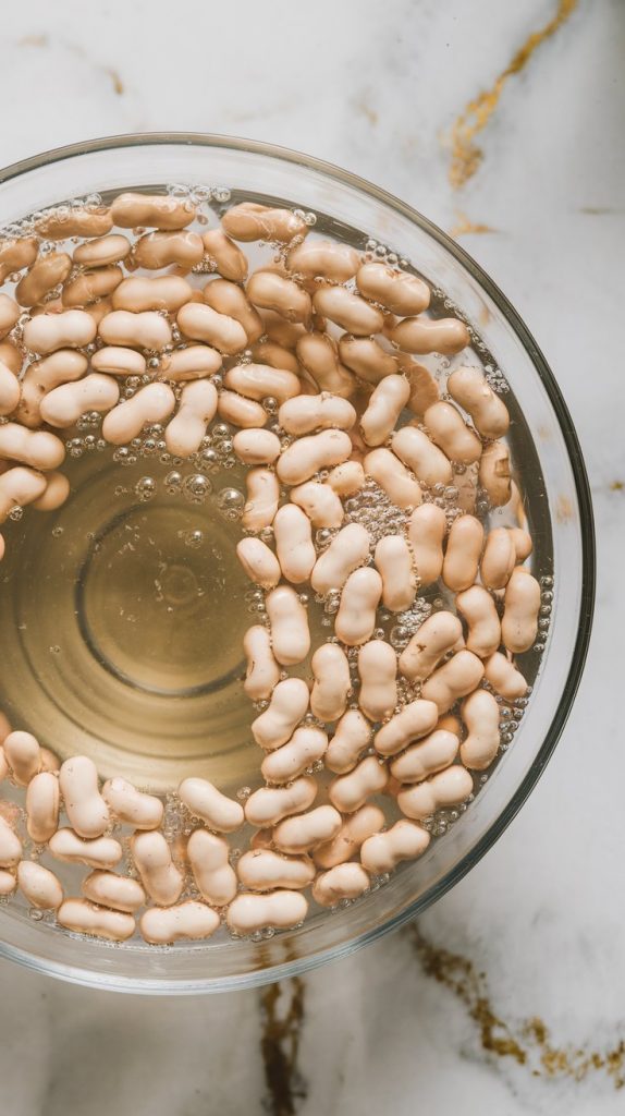 A large glass bowl filled with pinto beans soaking in water