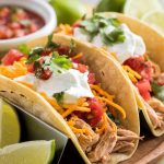 shredded chicken being spooned into a golden taco shell