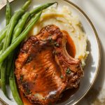 A plate of tender pork chops covered in a sticky, glossy sauce, served with mashed potatoes and steamed green beans