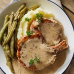 A plated dish of smothered pork chops with gravy, creamy mashed potatoes, and green beans