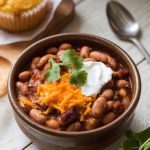 A serving of smoky pinto beans in a rustic ceramic bowl, topped with cheese, cilantro, and sour cream