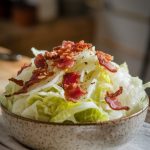 A serving of Crockpot Cabbage with Bacon and Onions in a rustic white bowl, garnished with crispy bacon bits