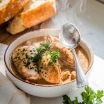 A steaming bowl of chicken stew garnished with chopped parsley