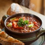 A bowl of hearty lentil soup with vibrant spinach and vegetables, topped with a slice of lemon on the side for garnish