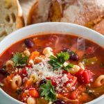 A steaming bowl of minestrone soup served with grated Parmesan and parsley on top