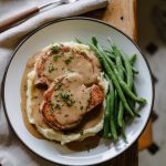 plated pork chops over mashed potatoes, smothered in gravy, garnished with parsley