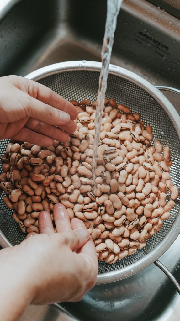 dried pinto beans being rinsed in a colander under running water