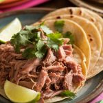 A vibrant taco spread with carnitas, lime wedges, fresh cilantro