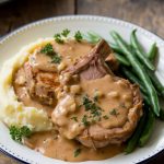 A serving of tender pork chops smothered in onion gravy, paired with creamy mashed potatoes and green beans