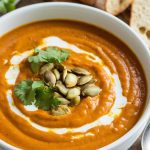 a bowl of Crockpot Pumpkin Curry Soup, garnished with cilantro, roasted pumpkin seeds