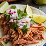 Crispy shredded carnitas loaded into warm tortillas with toppings like cilantro