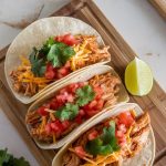 tacos being assembled: warm tortillas filled with shredded adobo chicken