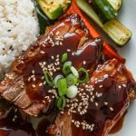 Tender short ribs served on a white plate, drizzled with glossy Korean BBQ sauce, and garnished with sesame seeds and green onions