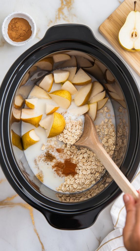 A crockpot filled with diced pears, steel-cut oats, milk, and spices