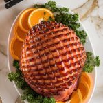 A golden, caramelized honey-baked ham served on a white platter