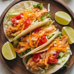 Freshly assembled tacos on a rustic wooden plate, filled with shredded chicken