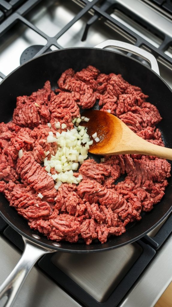 Ground beef browning in a large nonstick skillet with diced onions and minced garlic