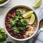 A bowl of pinto beans and rice topped with fresh cilantro and lime wedges