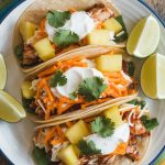 assembled tacos on a plate, each stuffed with chicken, pineapple, sour cream, cheese, and cilantro