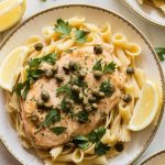 A plate of crockpot chicken piccata served over pasta, topped with fresh parsley and capers