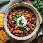 A steaming bowl of tender crockpot pinto beans topped with a sprinkle of fresh chopped cilantro and a dollop of sour cream