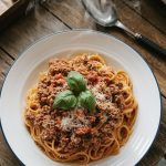 A serving of Italian ground beef over spaghetti, topped with fresh basil and grated Parmesan