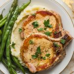 creamy garlic parmesan pork chops garnished with fresh parsley, served with mashed potatoes and green beans