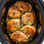 Honey garlic chicken in the slow cooker, garnished with sesame seeds and green onions