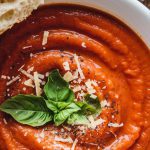 a bowl of creamy tomato basil soup garnished with fresh basil and Parmesan