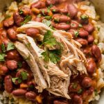 A steaming bowl of red beans and rice topped with shredded chicken, garnished with parsley