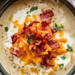 a steaming bowl of creamy cauliflower soup, topped with crispy bacon bits, shredded cheddar, and fresh parsley