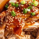 A slow cooker filled with shredded teriyaki chicken, glistening in a thick, glossy sauce