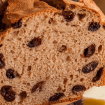 A fresh loaf of cinnamon raisin bread sits on a wooden cutting board