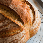 A freshly baked sourdough loaf resting on a wire cooling rack, golden and crispy