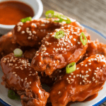 a plate of sweet chili chicken wings, garnished with sesame seeds and green onions