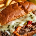 A fully assembled Slow Cooker Philly Cheesesteak Sandwich on a plate with crispy fries and a pickle